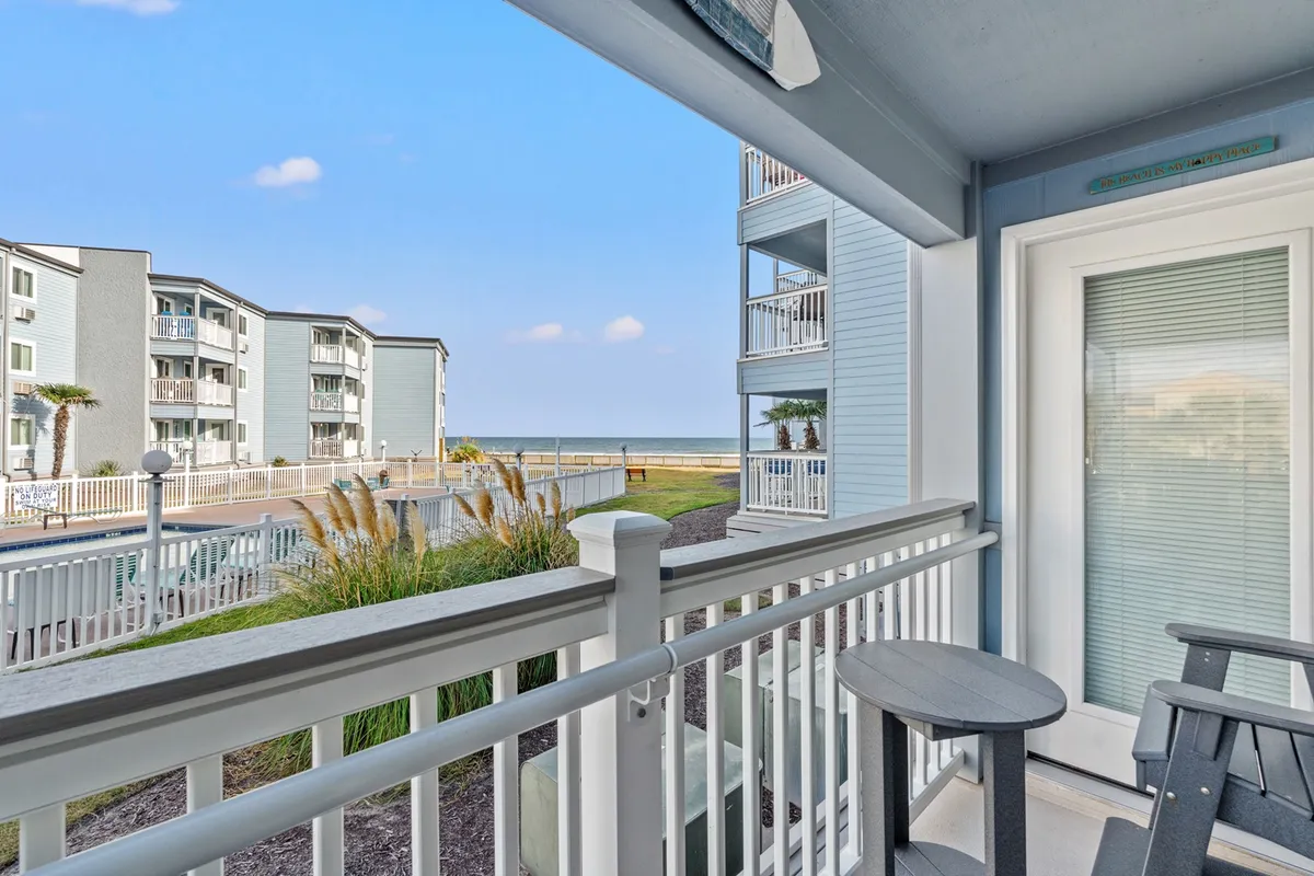 A serene balcony with comfortable seating that overlooks the beach, surrounded by lush greenery. The inviting outdoor space is perfect for coffee at sunrise or evening conversations with the ocean as a backdrop.