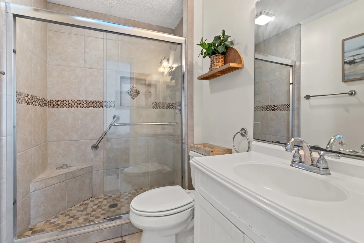 A stylish bathroom with a glass shower enclosure, modern sink and countertop, and a decorative wall-mounted plant shelf. The space feels fresh, inviting, and thoughtfully designed for comfort and privacy.